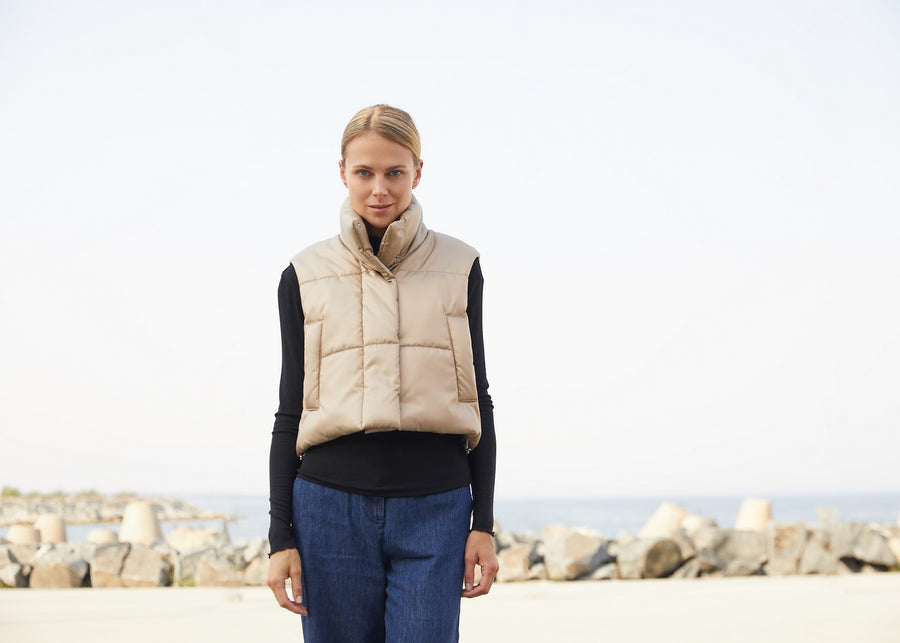 a woman wearing a cropped puffer vest with collar in gold color