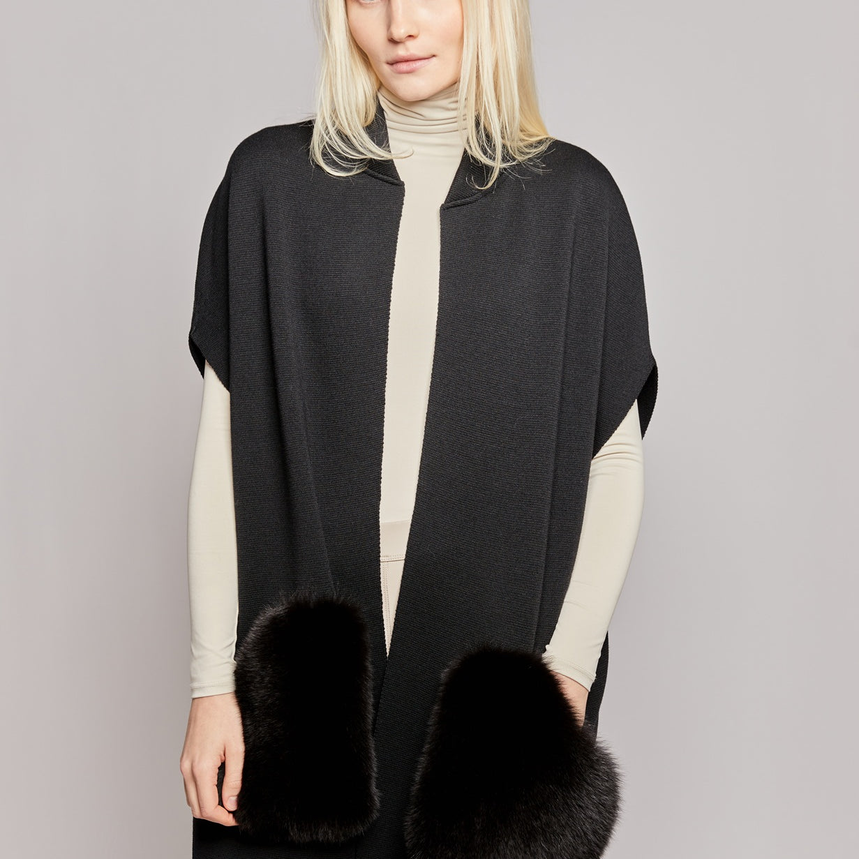 A woman wearing a black vest made from merino wool with luxurious fox fur pockets 