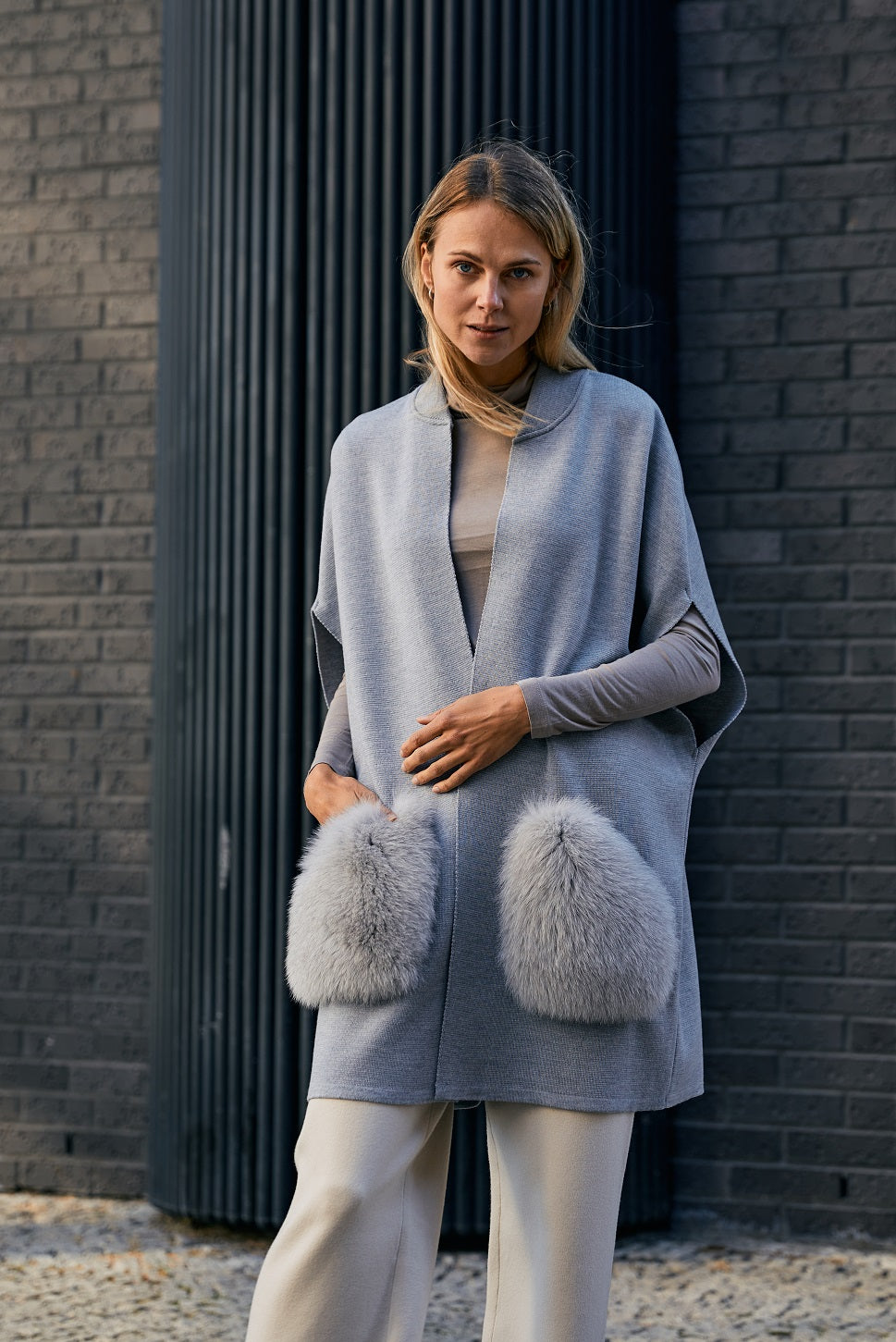 Woman wearing a grey merino knit vest with fox fur pockets 