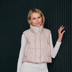 Woman wearing a light pink puffer vest against a dark background