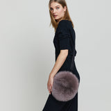 Lady modelling a Round fox fur cross-body and wrist bag.