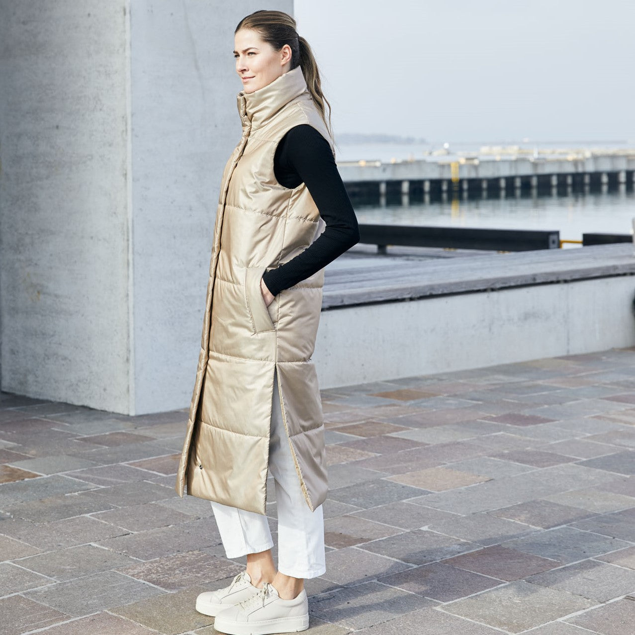 Lady modeling a limited edition vest is made from windproof and water repellent fabrics, with a soft down-like nonwoven lining. The vest has a collar and push button closing. 