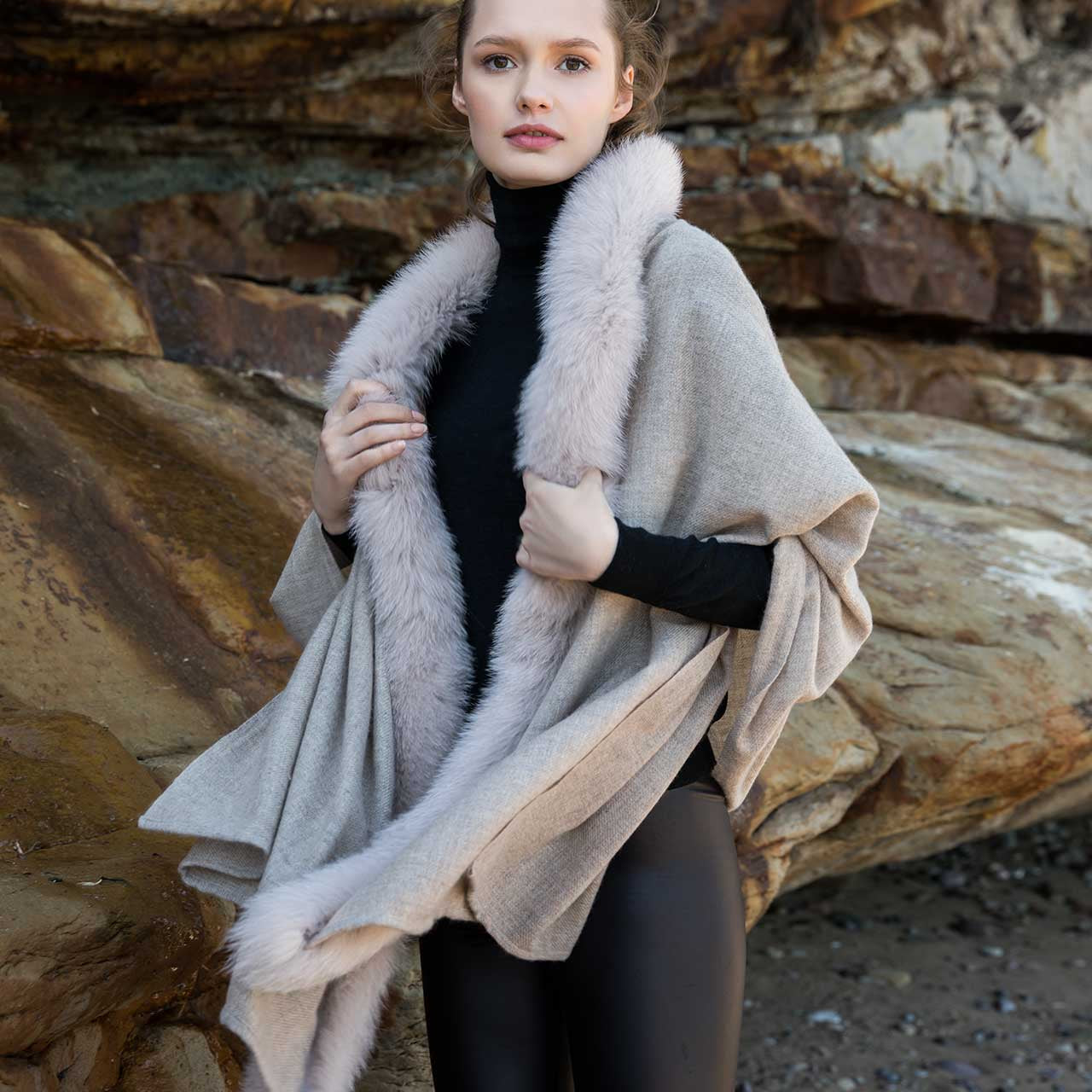 Young woman standing on a beach wearing a beige Gemmi cashmere wrap with fox fur