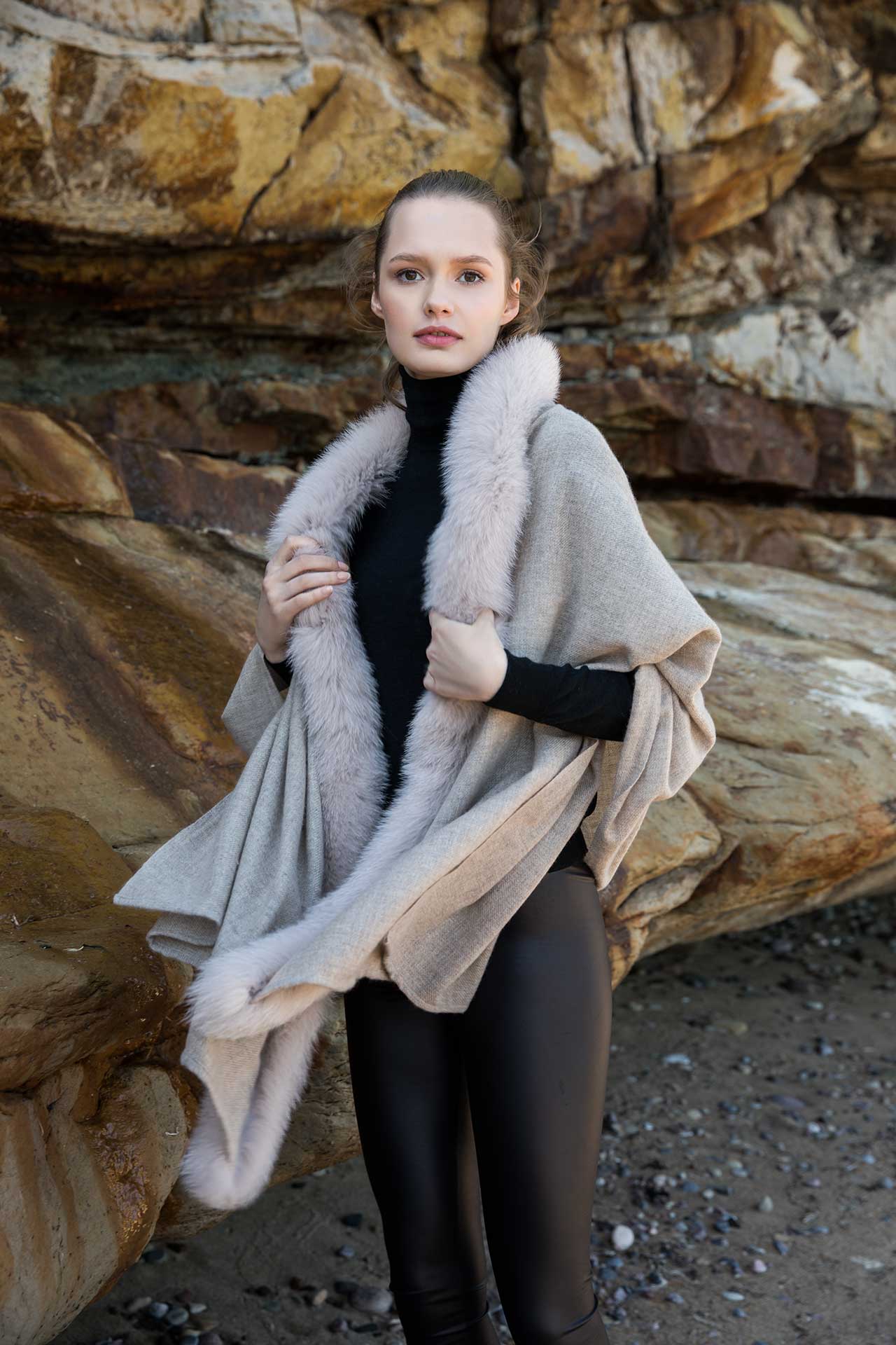 Young woman standing on a beach wearing a beige Gemmi cashmere wrap with fox fur